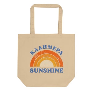 Peut inclure: Un sac fourre-tout beige avec un motif arc-en-ciel et le texte "Kalhmera Sunshine" en bleu.