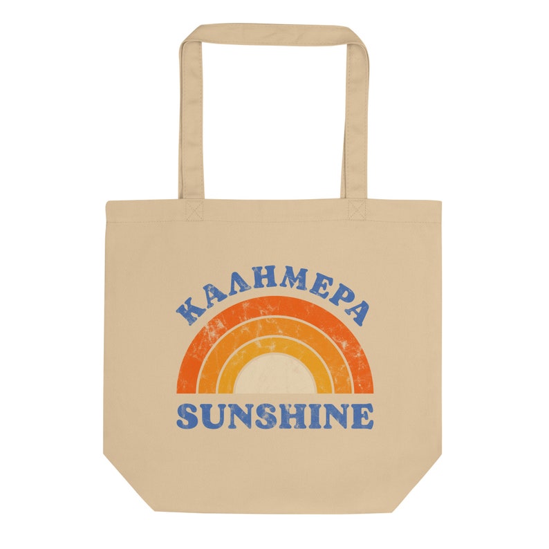 Peut inclure: Un sac fourre-tout beige avec un motif arc-en-ciel et le texte "Kalhmera Sunshine" en bleu.
