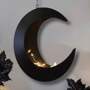 Puede incluir: Decoración de pared de metal negro en forma de media luna con un diseño recortado y luces de cadena en el interior.