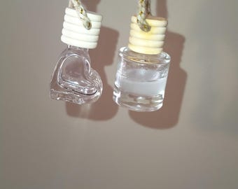 May include: Two glass car air fresheners hanging from a string. One is a heart-shaped bottle and the other is a round bottle. Both bottles are clear and filled with a liquid.