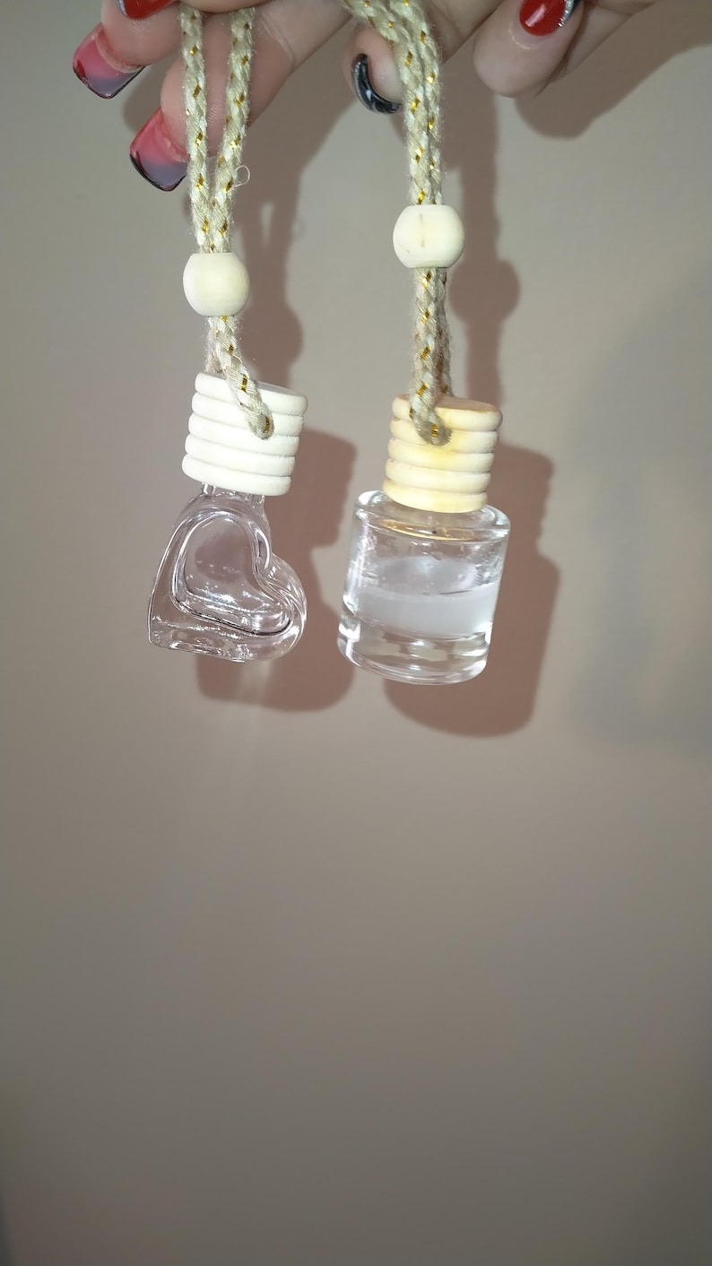 K&ouml;nnte beinhalten: Zwei gl&auml;serne Auto-Lufterfrischer, die an einer Schnur h&auml;ngen. Einer ist eine herzf&ouml;rmige Flasche und der andere eine runde Flasche. Beide Flaschen sind klar und mit einer Fl&uuml;ssigkeit gef&uuml;llt.