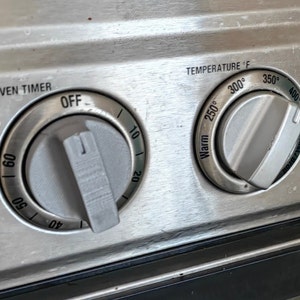 May include: Close-up of a stainless steel oven control panel with three knobs. The knobs are labeled "ON/OVEN TIMER", "OFF", and "TEMPERATURE °F". The temperature knob has markings for "Warm", "250°", "300°", "350°", and "400°".