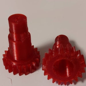 Puede incluir: Dos engranajes de pl&aacute;stico rojo con forma cil&iacute;ndrica. Los engranajes tienen una superficie lisa y un borde dentado.