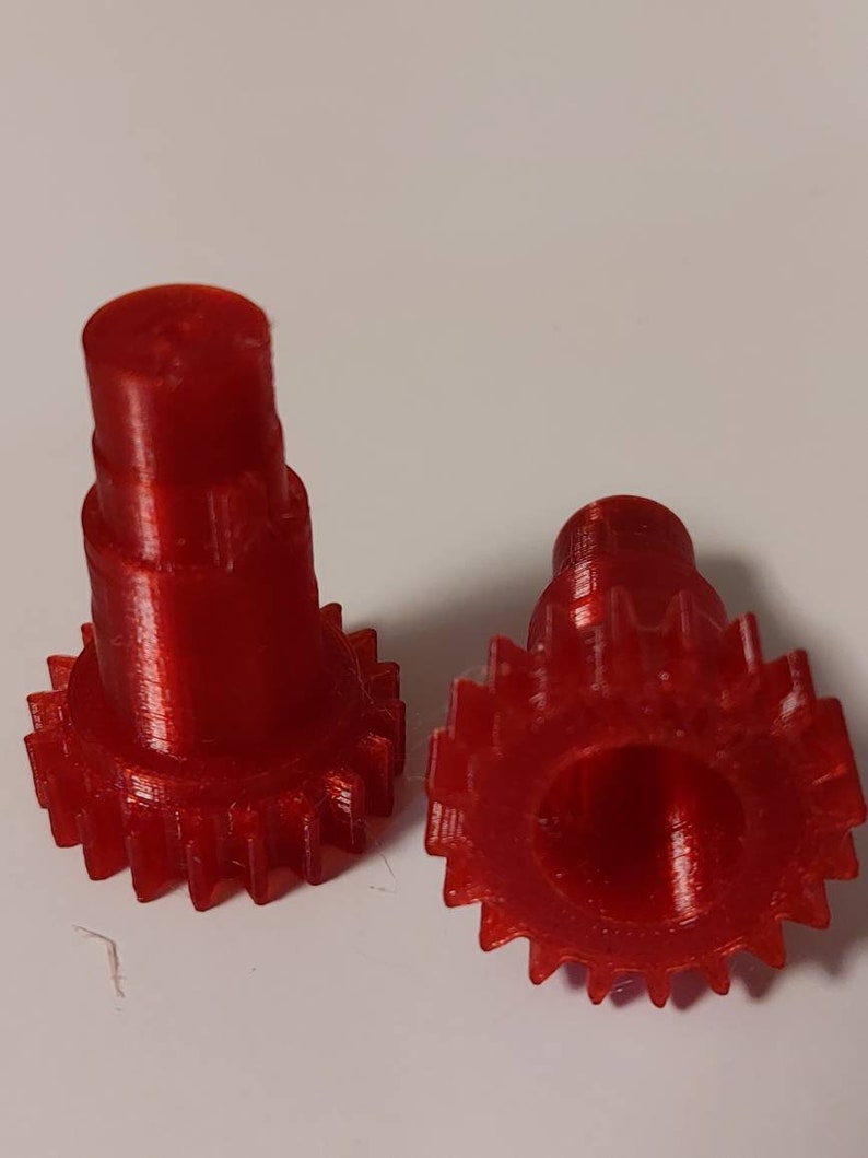 Puede incluir: Dos engranajes de pl&aacute;stico rojo con forma cil&iacute;ndrica. Los engranajes tienen una superficie lisa y un borde dentado.