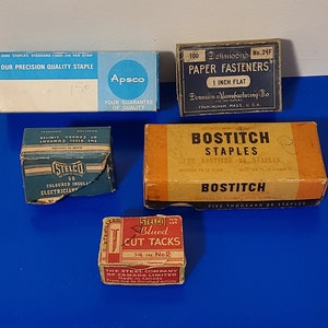 Puede incluir: Surtido de cajas vintage de suministros de oficina, que incluyen grapas, sujetapapeles y chinchetas. Las cajas son de varios colores, incluidos azul, rojo, amarillo y blanco. Las cajas tienen texto en ellas, incluidos los nombres de las marcas "Apsco", "Dennison", "Bostitch" y "STELCO".