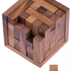 Könnte beinhalten: Ein 3D-Holzpuzzle mit einem komplexen Design. Das Puzzle besteht aus vielen kleinen Holzblöcken, die ineinandergreifen, um einen Würfel zu bilden. Das Puzzle ist in einem zerlegten Zustand, wobei die Blöcke um den Würfel herum verstreut sind. Das Puzzle ist aus Naturholz gefertigt und hat eine rustikale Oberfläche.