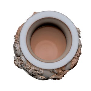 Pu&ograve; includere: Vista dall'alto di un vaso decorativo con un ampio bordo bianco e un interno marrone chiaro. L'esterno presenta decorazioni floreali e a volute in rilievo ornate, nei toni del beige e del grigio. Il vaso ha un'estetica classica ed elegante.