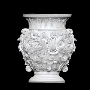 Pu&ograve; includere: Un vaso bianco e ornato con intricati dettagli floreali e a volute. Il vaso presenta un bordo ampio e dettagliato e una base a piedistallo. Il design include rose e altri fiori stilizzati, creando un'estetica classica.