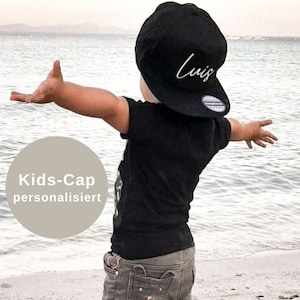 Könnte beinhalten: Eine schwarze Baseballkappe mit dem in weißer Schreibschrift gestickten Namen Luis auf der Vorderseite, kombiniert mit einem schwarzen kurzärmeligen T-Shirt und einer grauen Jeansshorts mit Taschendetails. Die Kappe hat einen runden Aufkleber.