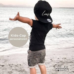Könnte beinhalten: Eine schwarze Baseballkappe mit dem in weißer Schreibschrift gestickten Namen Luis auf der Vorderseite, kombiniert mit einem schwarzen kurzärmeligen T-Shirt und einer grauen Jeansshorts mit kleinen Taschendetails. Die Kappe hat einen flachen Schirm.