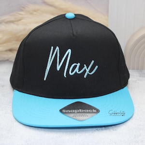 May include: Black and light blue Snapback hat with the name "Max" embroidered in light blue script. The hat features a flat brim and a snap closure. A small, light blue button is on top of the hat.