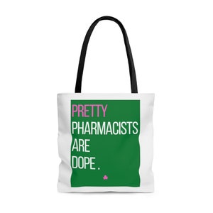 May include: White tote bag with black handles featuring the text "PRETTY PHARMACISTS ARE DOPE." in pink and white letters on a green background. A small pink star is at the bottom. The bag is designed for carrying items.