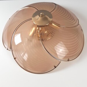 May include: A vintage ceiling light fixture with a unique design. The light has a circular shape with multiple curved, petal-like sections made of translucent, light brown glass. The sections are outlined with a metal frame and converge at a central, gold-colored fixture.