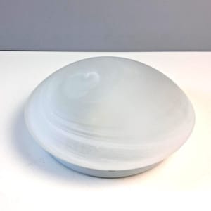 Könnte beinhalten: Eine runde, kuppelförmige Deckenleuchte mit einem mattweißen Glasschirm, der dezente, wirbelnde, durchscheinende Muster aufweist. Die Glaskuppel ist auf einem einfachen, kreisförmigen Metallsockel montiert und bildet ein funktionales Beleuchtungselement.
