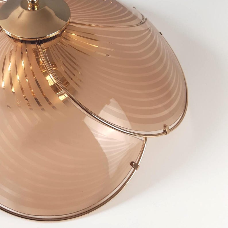May include: A vintage ceiling light fixture with a gold-toned metal frame and a peach-colored glass shade. The shade features a series of curved, etched lines. The fixture is designed to be mounted on a ceiling.