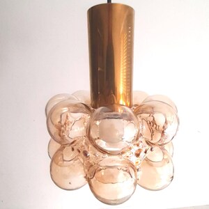 May include: A pendant light fixture featuring a cylindrical metallic gold top section connected to a cluster of spherical, translucent amber-colored glass orbs that form a rounded, bubble-like shape around the central light source.