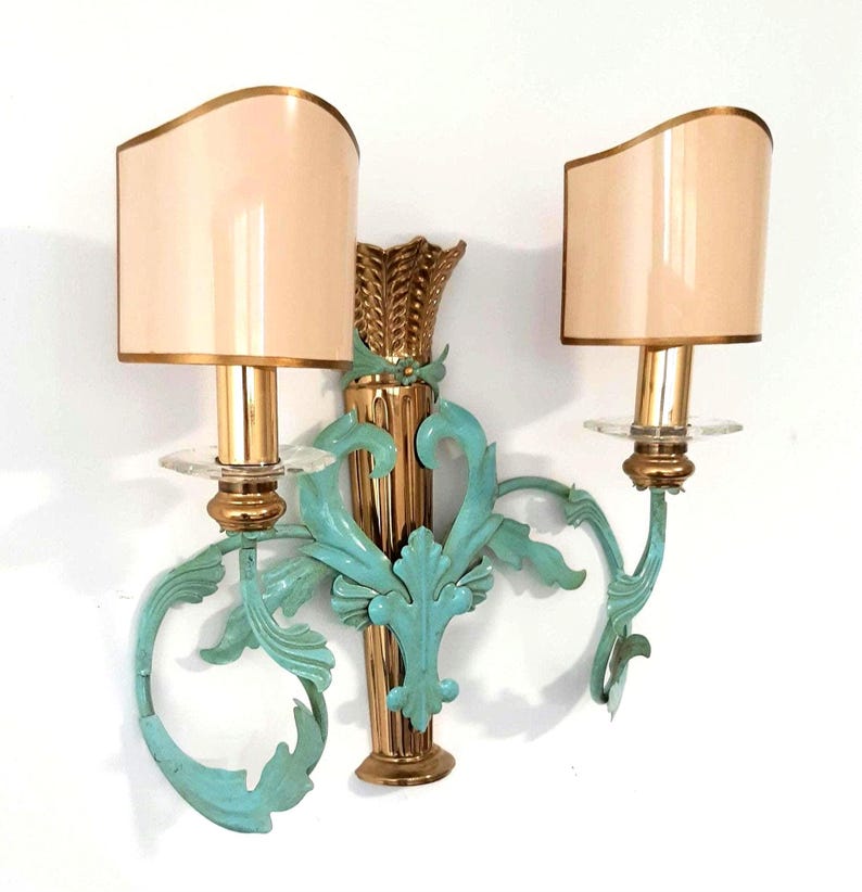 May include: A pair of wall sconces with a gold finish and teal accents. Each sconce features a beige lampshade with a gold trim. The sconces have a decorative wheat stalk design and ornate teal leaf details.