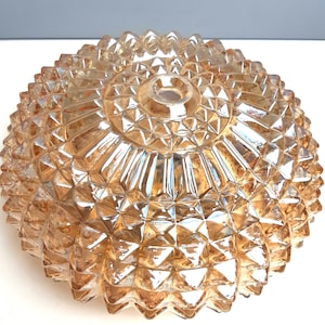 Könnte beinhalten: Ein vintage, bernsteinfarbener Glas-Leuchtenabdeckung. Die Abdeckung hat eine abgerundete, schalenförmige Form mit einem strukturierten, geometrischen Muster. Das Glas ist transparent und lässt Licht durch. Die Leuchte hat ein zentrales Loch zur Montage.