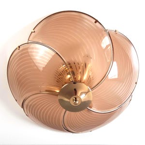May include: A decorative ceiling light fixture with a flower-like design. The fixture features six petal-shaped panels made of translucent, peach-colored glass with a striped pattern. The panels are held together by a gold-colored metal frame and a central gold-colored base.