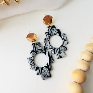 May include: A pair of black and white geometric earrings with a gold accent. The earrings are made of polymer clay and have a unique, abstract design.