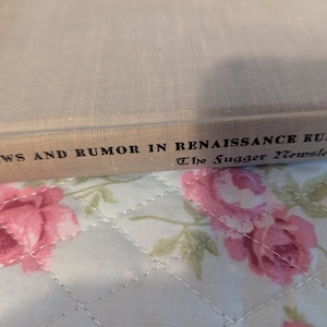 Könnte beinhalten: Ein Hardcover-Buch mit dem Titel "News and Rumor in Renaissance Europe" mit "The Fugger Newsletters" darunter gedruckt. Das Buch hat einen hellbeigen Leinenumschlag. Der Hintergrund ist ein Blumenmuster mit rosa Rosen.
