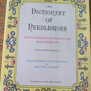 Könnte beinhalten: Ein Vintage-Buch mit dem Titel "The Dictionary of Needlework" mit gelbem Einband und Zierbordüre. Der Einband zeigt Text in einer klassischen Schrift, einschließlich der Namen der Autoren und des Satzes "Faksimile der Ausgabe von 1882."