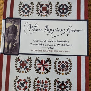 May include: A book titled "Where Poppies Grow: Quilts and Projects Honoring Those Who Served in World War I" by Dennielle Bohannon and Janice Britz. The cover features a red, white, and blue quilt block design with a wreath of leaves around it.