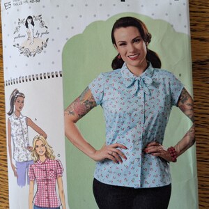 May include: Simplicity sewing pattern S9295. The pattern features a woman wearing a light blue blouse with a floral print and a bow. The pattern also shows illustrations of other blouse styles. The text "easy-to-sew" is visible.