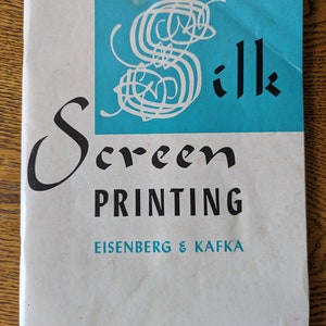 Puede incluir: Un libro blanco con una cubierta azul. La cubierta tiene una "S" estilizada blanca con la palabra "Silk" en texto negro. El título del libro es "Screen Printing" en texto negro. El nombre del autor es "Eisenberg & Kafka" en texto negro.