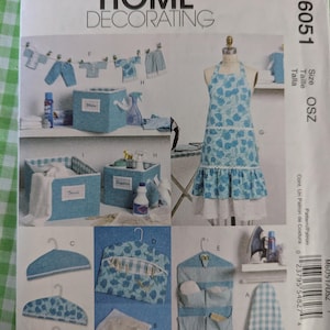 Puede incluir: Patrón de costura McCall's Home Decorating. La imagen muestra varios artículos de decoración para el hogar, incluyendo un delantal, cajas de almacenamiento, perchas y un organizador colgante. Los artículos son en tonos azules y blancos, con estampados florales y cuadros vichy.