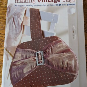 Może przedstawiać: Książka zatytułowana "Making Vintage Bags" z 20 oryginalnymi wzorami szycia do vintage'owych toreb i portfeli. Okładka przedstawia zbliżenie brązowej i złotej vintage'owej torebki ze srebrną klamrą.