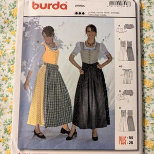 May include: A Burda 8448 sewing pattern envelope for a dirndl dress. The front displays two variations of the dress: one with a yellow bodice and a split yellow and green plaid skirt, and another with a beige bodice and a dark patterned skirt.