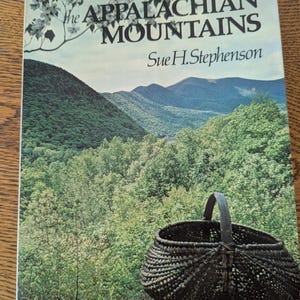 May include: A book cover titled "Basketry of the Appalachian Mountains" by Sue H. Stephenson. The cover features a woven basket in the foreground, with a scenic mountain landscape in the background.