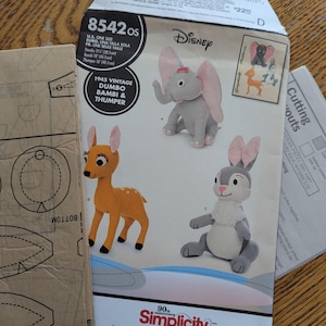 May include: Simplicity sewing pattern 8542 OS featuring Disney's Dumbo, Bambi, and Thumper. The pattern includes instructions for making plush toys. Dumbo is 11 inches (28.5cm), Bambi is 18 inches (45.5cm), and Thumper is 16 inches (40.5cm).