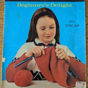 以下が含まれることがあります： ヴィンテージのSpinnerin Beginner's Delight編み物パターンブックレット、ボリュームNo.308。表紙には赤い毛糸で編み物をしている人物が描かれており、101 IDEASおよびPRICE 50 CENTSという文字が見えます。背景は鮮やかな青色で、白いアクセントが施されています。