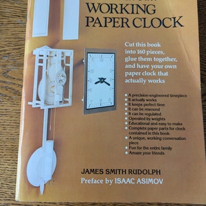 Pode incluir: Uma capa de livro com fundo amarelo e uma ilustração em preto e branco de um relógio de papel. O título é "Make Your Own Working Paper Clock". O livro é de James Smith Rudolph com um prefácio de Isaac Asimov.