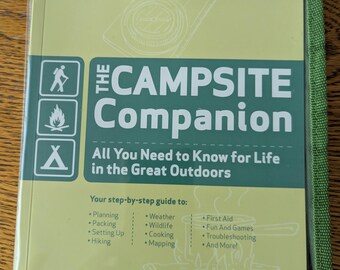 May include: A green and yellow book titled "The Campsite Companion" with a compass graphic. The book cover includes text about outdoor life, planning, and first aid. The book is encased in a green fabric cover.