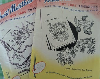 May include: Two vintage Aunt Martha's Hot Iron Transfer packets. One features a floral design, the other has vegetable-themed designs with text like "Pumpkins Sunday" and "Onions Monday". The packets are for needlework and textile crafts.