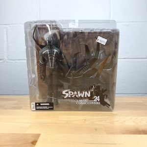 May include: A Spawn action figure from the Classic Comic Covers series, number 24, in its original packaging. The figure is dark with white accents and comes with accessories. The packaging is clear plastic.
