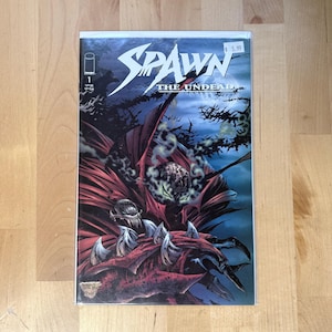 May include: A comic book titled "Spawn The Undead" with a cover featuring a dark, detailed illustration of a demonic figure in red and black. The comic is in a protective sleeve.