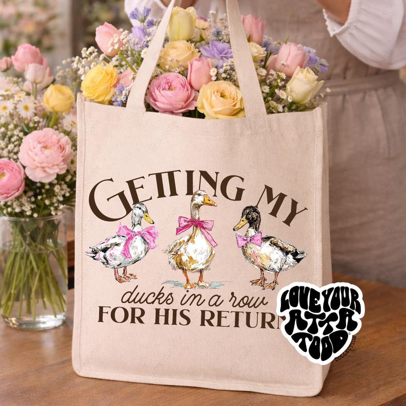 Natural cotton canvas tote featuring three illustrated ducks wearing pink bows with text “GETTING MY ducks in a row FOR HIS RETURN” on front and personalized back reading “LOVED BY JESUS CARRIED BY – NAME –”, customizable Christian church tote gift for mom, friend, teacher, or teen girl.