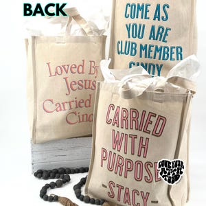 May include: Three canvas tote bags with various phrases printed on them. One says "Loved By Jesus Carried Cindy", another reads "Come As You Are Club Member Cindy", and the third says "Carried With Purpose - Stacy".