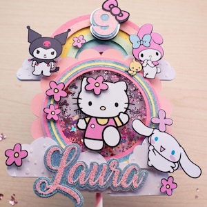 May include: A multi-layered cake topper featuring a central shaker element with Hello Kitty, surrounded by Kuromi, My Melody, and Cinnamoroll characters. The design includes a rainbow, pink flowers, clouds, a glittery number 9, and the name Laura in script.