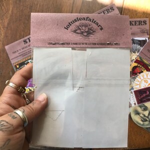 May include: A pack of vintage witchy stickers with a variety of designs, including a sun, a moon face, and a card that says "CARDS". The stickers are hand-cut in the UK from authentic vintage pieces. The pack is labeled "Lotusleafaltars".