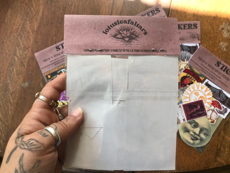 May include: A pack of vintage witchy stickers with a variety of designs, including a sun, a moon face, and a card that says "CARDS". The stickers are hand-cut in the UK from authentic vintage pieces. The pack is labeled "Lotusleafaltars".