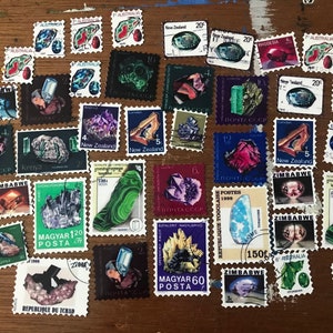 Puede incluir: Una colección de sellos postales coloridos con imágenes de piedras preciosas y minerales. Se ven sellos de Australia, Nueva Zelanda, Zimbabue y otros países. Los sellos están dispuestos sobre una superficie de madera.
