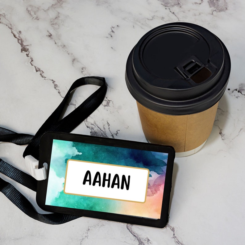 May include: A black lanyard with a colorful watercolor background name tag that says "AAHAN". The name tag is on a white marble surface next to a brown paper cup with a black lid.