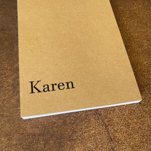 K&ouml;nnte beinhalten: Ein braunes Notizbuch mit dem Namen "Karen" auf dem Einband.