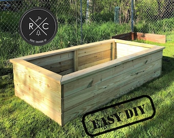 May include: A wooden raised garden bed with a natural wood finish. The bed is surrounded by green grass and a chain link fence. The text "EASY DIY" is stamped in black on the lower right corner of the image.