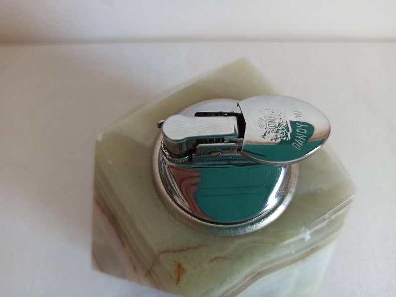 Puede incluir: Un encendedor de mesa de m&aacute;rmol verde con una tapa plateada. La tapa tiene las palabras "DANDY" y "LONDON" grabadas.